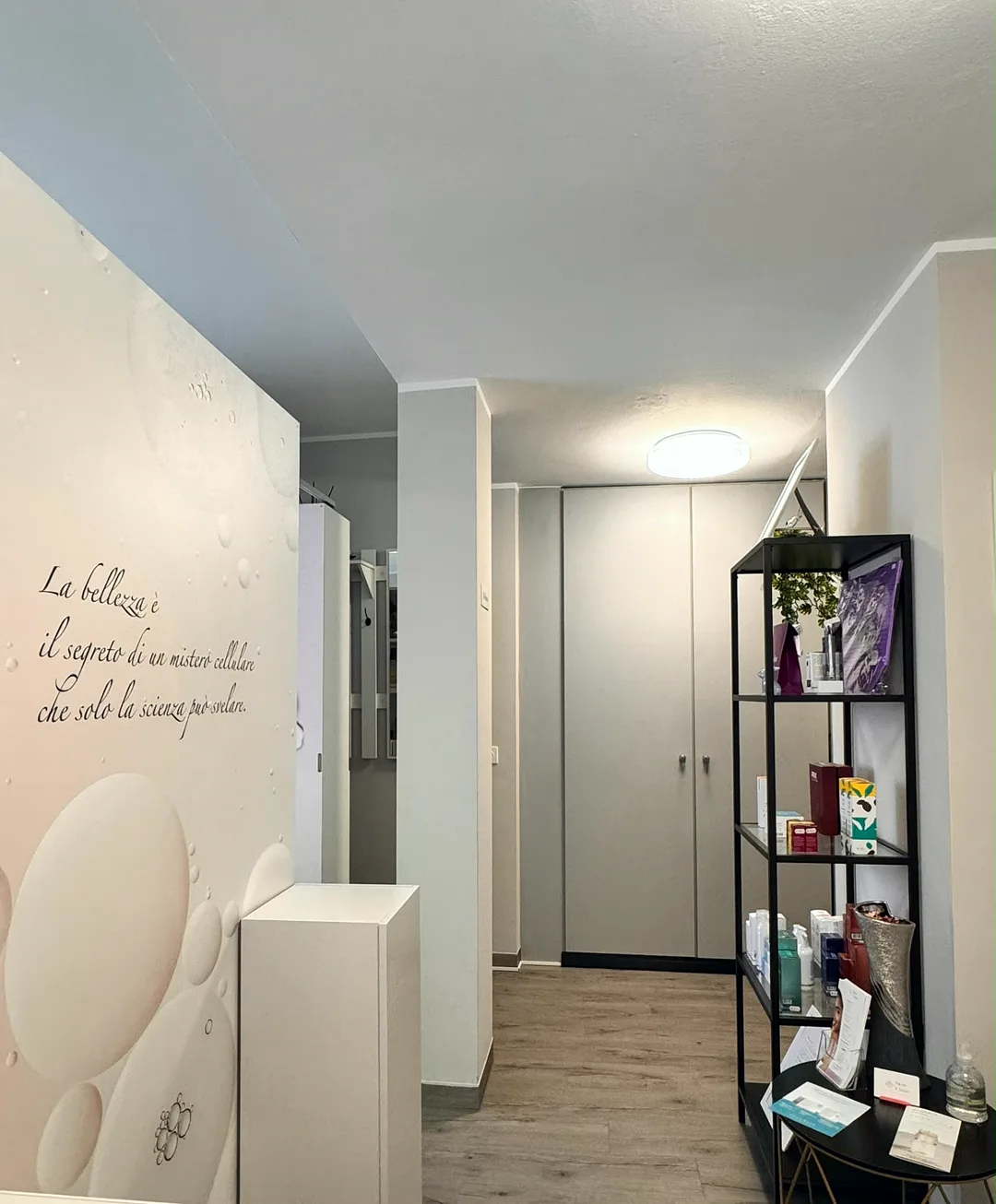 Corridoio di Skin Clinic con parete decorativa rosa, frase sulla bellezza ed espositore di prodotti